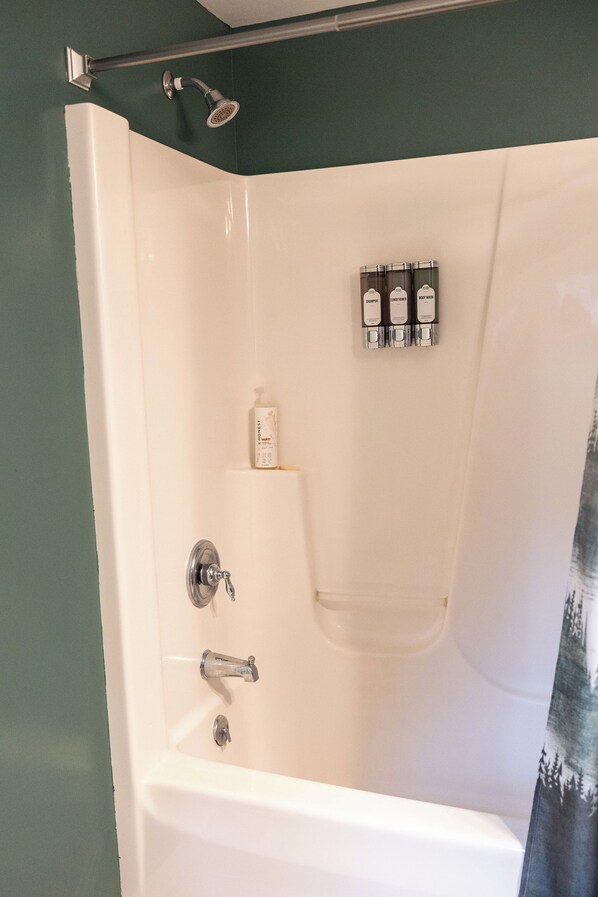 A white bathtub with a showerhead, a soap dispenser, and a set of toiletries on a shelf.