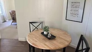 Een eetgedeelte met een ronde houten tafel, twee stoelen, een potplant en een lijst met een foto aan de muur.