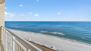 A beach view from a balcony with a railing, clear sky, and calm sea. - Indigo West 1404 (Pensacola)