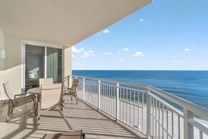 Un balcone con vista sull'oceano, un tavolo, sedie e una porta che dà su una stanza.
