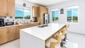 A modern kitchen with wooden cabinets, a large island, and bar stools. - New Unique Villa Blue Top! 2 Bedrooms Waterfront with Kayak (Bay, Cooper Jack)
