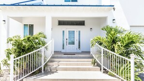 A white building with a front porch, a set of stairs leading to the entrance, and two large potted plants on either side. - New Unique Villa Blue Top! 2 Bedrooms Waterfront with Kayak (Bay, Cooper Jack)