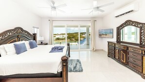 A bedroom with a large bed, two ceiling fans, a dresser, and a view of a beach through a sliding glass door. - New Unique Villa Blue Top! 2 Bedrooms Waterfront with Kayak (Bay, Cooper Jack)