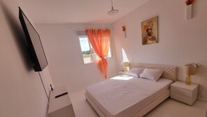 A bedroom with a bed, bedside tables, a TV mounted on the wall, and a window with curtains.