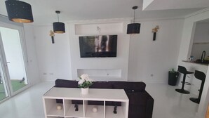 A modern living room with a white console table, black sofa, and a flat-screen TV mounted on the wall.