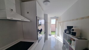 A modern kitchen with white cabinetry, a black mat at the entrance, and a view of a garden through an open door.