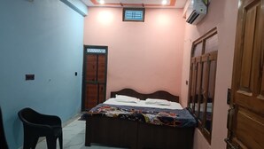 A small bedroom with a bed, a chair, a window, and a door. - Chandrika Palace - Best Hotel Near Ram Mandir (Ayodhya)
