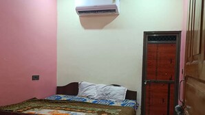A bedroom with a bed, a ceiling fan, an air conditioner, and a door with a metal gate. - Chandrika Palace - Best Hotel Near Ram Mandir (Ayodhya)