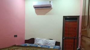 A bedroom with a bed, a ceiling fan, an air conditioner, and a door with a metal mesh. - Chandrika Palace - Best Hotel Near Ram Mandir (Ayodhya)