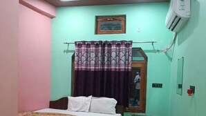 A bedroom with a bed, a small table, a ceiling fan, and an air conditioning unit. - Chandrika Palace - Best Hotel Near Ram Mandir (Ayodhya)