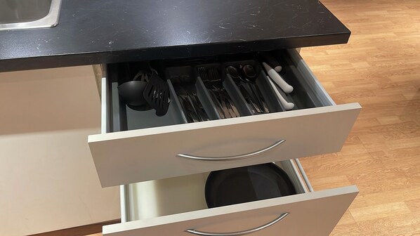A kitchen drawer with utensils and a black countertop.