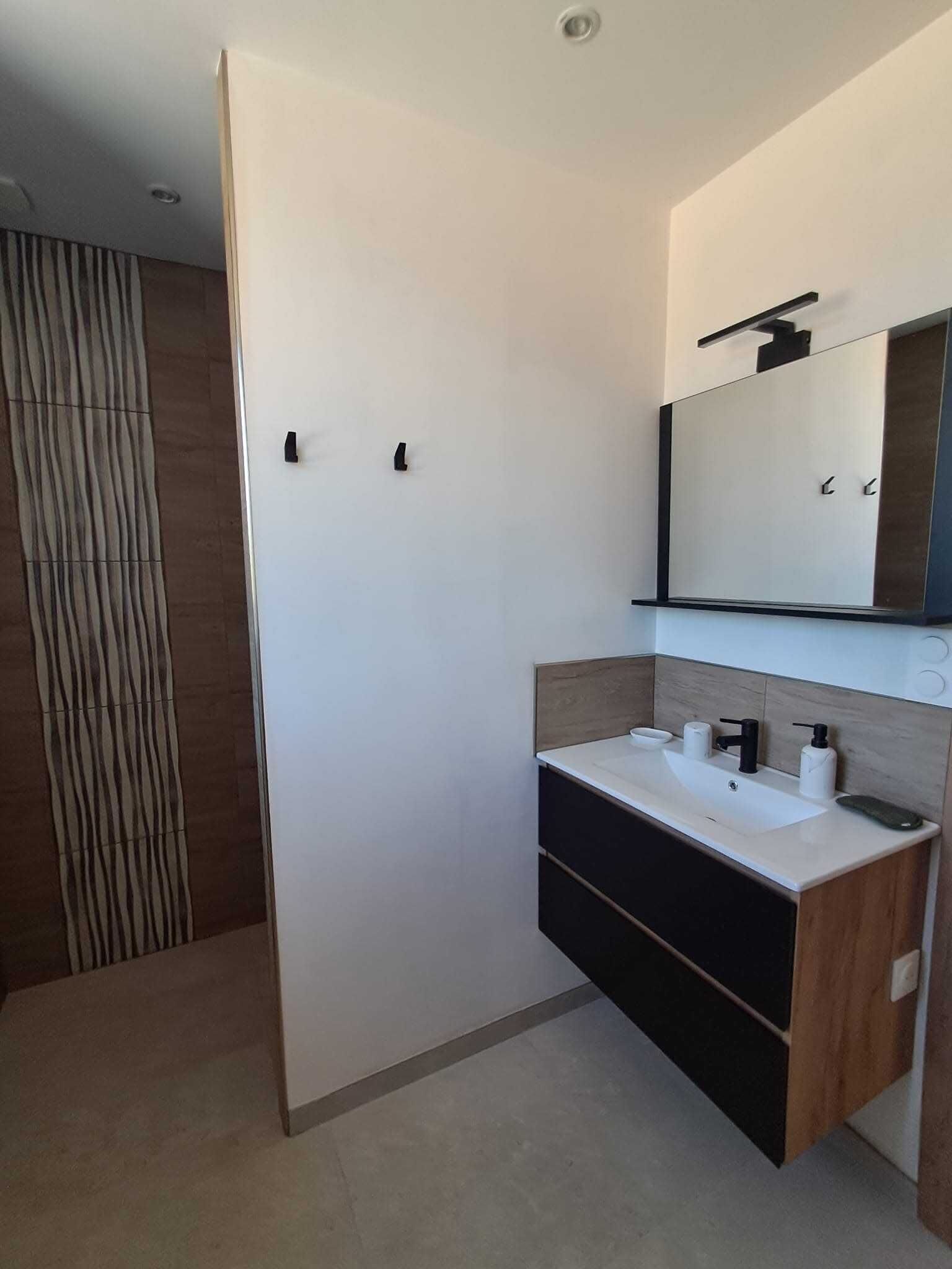 Un baño moderno con un lavamanos blanco, un mueble negro y un espejo grande.