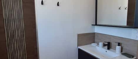 Un baño moderno con un lavamanos blanco, un mueble negro y un espejo grande.