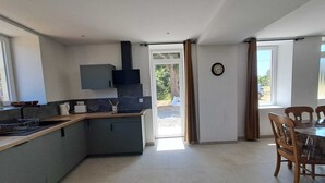 A modern kitchen with grey cabinets, a wooden countertop, and a built-in stove. There is a dining area with a table and chairs, and a window providing natural light. - Maison neuve 2 chambres au calme à Ceaulmont (Ceaulmont)