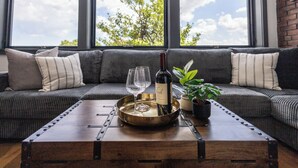 A modern living room with a sofa, a wooden coffee table with a tray, a bottle of wine, and a potted plant. - Entire House Free Parking/Sleeps 26/MIT/Harvard/TD (Somerville)