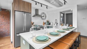 A modern kitchen with a central island, stainless steel appliances, and a brick accent wall. - Entire House Free Parking/Sleeps 26/MIT/Harvard/TD (Somerville)