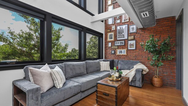A modern living room with a grey sofa, wooden coffee table, and a brick wall with framed pictures. - Entire House Free Parking/Sleeps 26/MIT/Harvard/TD (Somerville)