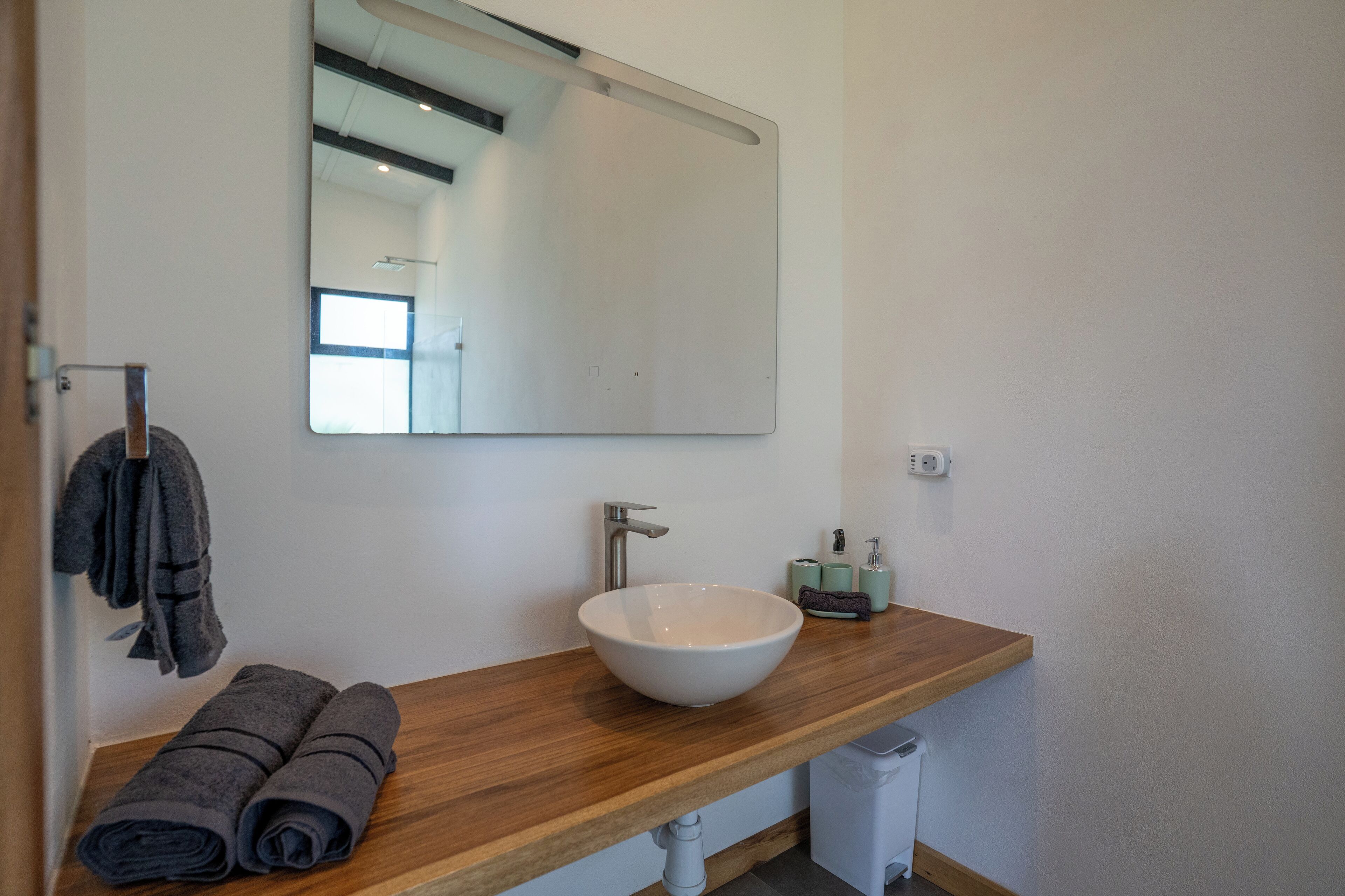 A bathroom with a wooden vanity, a white sink, a mirror, and towels.