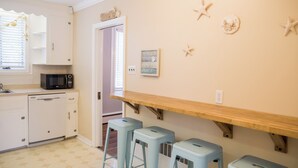 Una cucina con mobili bianchi, un forno a microonde e uno scaffale in legno sopra tre sgabelli azzurri.