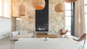A modern living room with a stone wall, a fireplace, and wicker pendant lights.