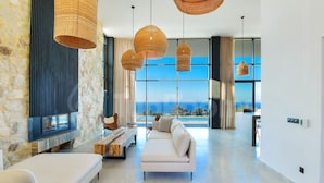 A modern living room with a stone wall, a fireplace, a sofa, and a view of the ocean.