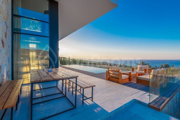 A modern outdoor terrace with a pool, wooden furniture, and a glass railing overlooking a scenic landscape.
