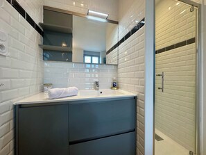 A modern bathroom with white subway tile walls, a white sink, and a dark-colored cabinet.