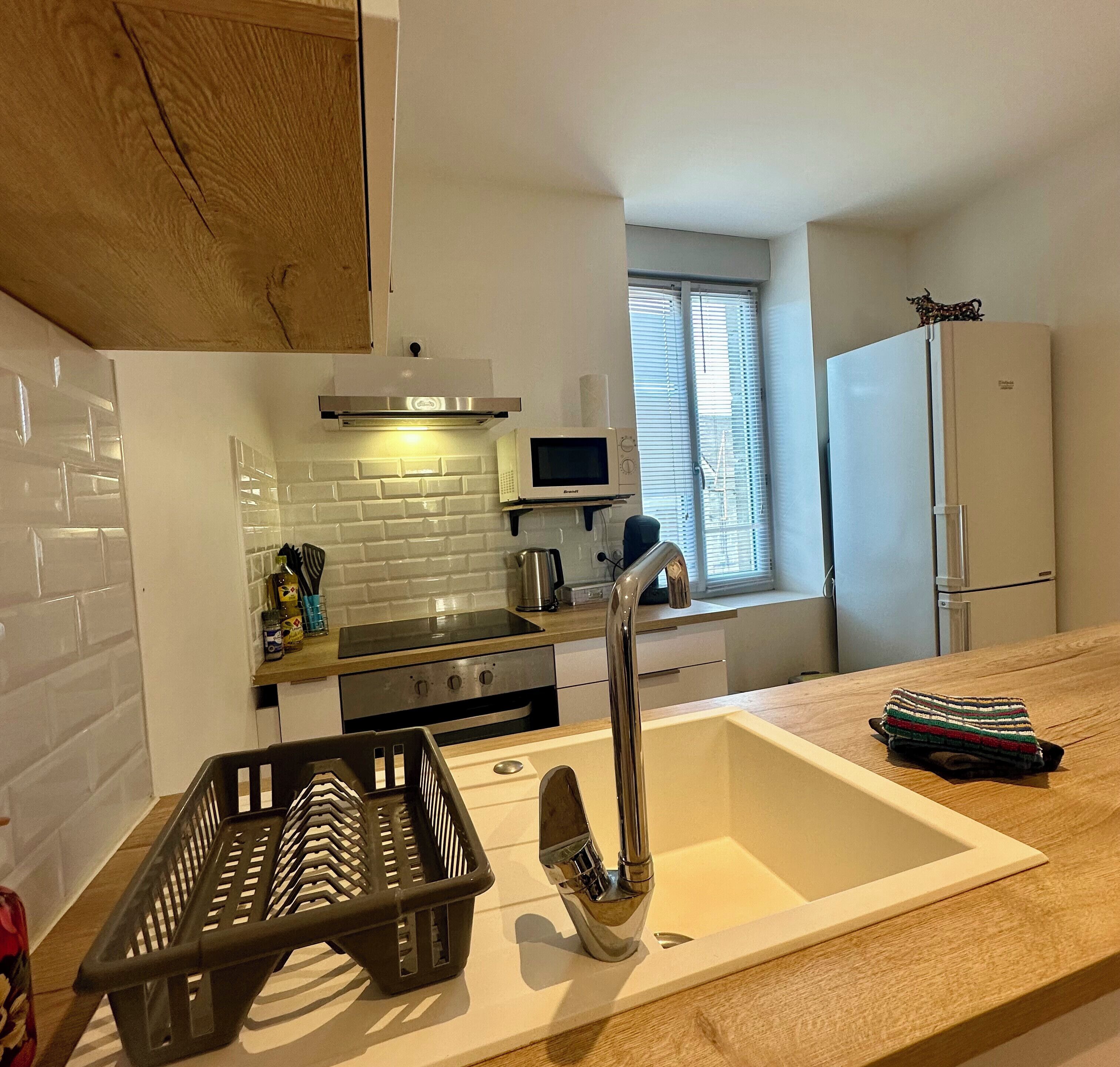 Una cocina moderna con azulejos tipo metro blancos, electrodomésticos de acero inoxidable y un ventanal con persianas.