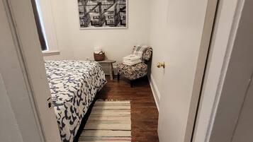 A bedroom with a bed, a chair, a small table, a rug, and a wall-mounted picture.