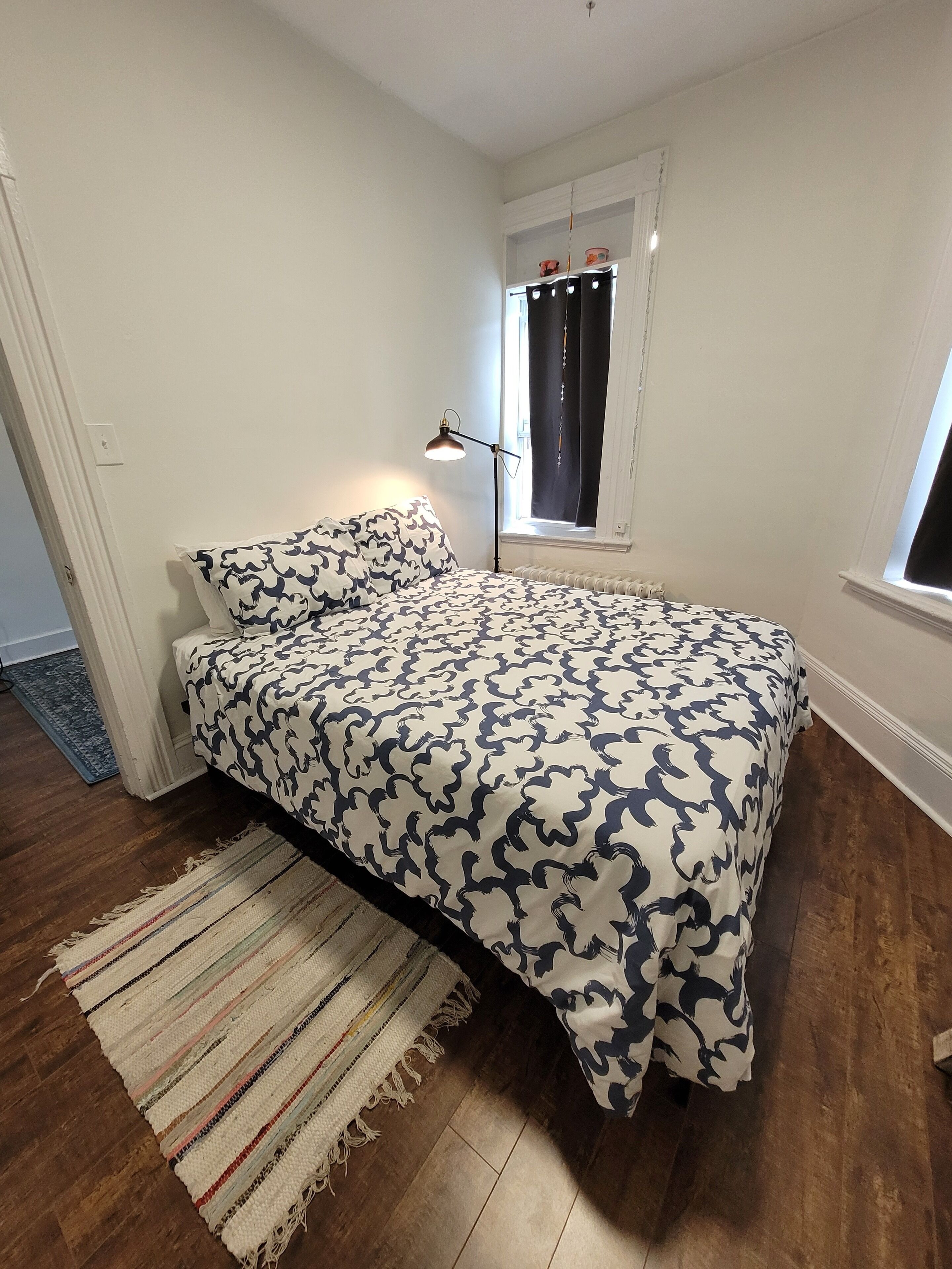 Une chambre à coucher avec un lit, une fenêtre avec des rideaux, une lampe de sol et un tapis.