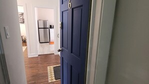 En hall som leder till ett kök med en blå dörr, trägolv och ett kylskåp i rostfritt stål.