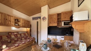 Ett mysigt rum med trämöbler, ett matbord för fyra personer och en köksdel med träskåp och köksutrustning.
