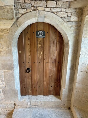 Une porte en bois surmontée d’un arc en pierre, avec une sonnette en laiton et une enseigne au-dessus de la porte.