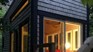 A wooden cabin with a porch, a door leading inside, and a visible interior with a red object.