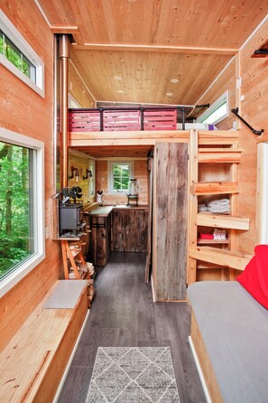 Une petite cabane en bois, dotée d’un coin cuisine, d’un lit et offrant une vue sur la forêt.
