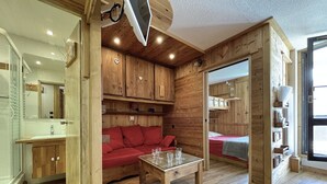 Ein gemütliches Blockhauszimmer mit Holzvertäfelung, einem roten Sofa, einem kleinen Tisch mit Gläsern und einem Etagenbett.