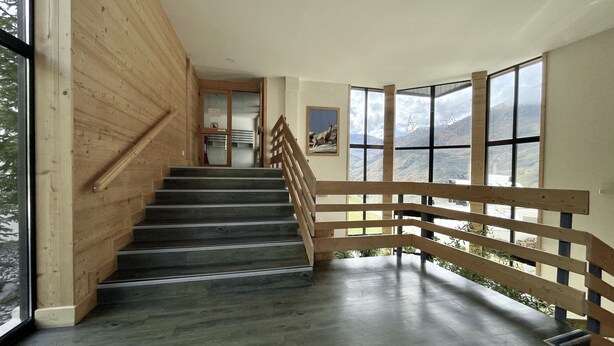 Eine Treppe mit Holzwangen führt zu einem Raum mit großen Fenstern und Bergblick.