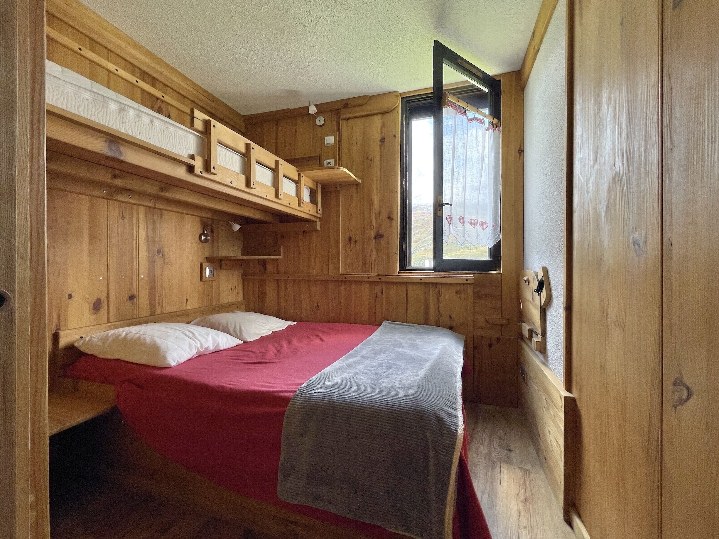 Une pièce aménagée comme un chalet en bois, avec un lit superposé, une fenêtre avec des rideaux et une tête de lit en bois.