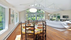 A spacious living room with a large white sectional sofa, a dining area with a round table and chairs, and large windows offering a view of greenery. - Charming 3-bedroom Ranch in Weston Near Westport & Fairfield (Weston)