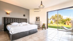 A modern bedroom with a large bed, a view of the outdoors, and a ceiling light fixture. - Villa Aigue Marine - Front de mer (Coti-Chiavari)