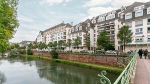 Une vue sur la rivière, avec des immeubles résidentiels à plusieurs étages, un mur de briques et une rambarde métallique verte le long du sentier.