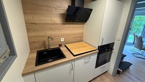 A modern kitchen with a wooden backsplash, a black sink, a wooden cutting board, and a built-in oven. - Haus Majda - A place with heart, history and friendship (Ronshausen)