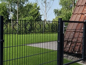 A gated area with a grassy lawn and a pathway leading to a building with a metal roof. - Haus Majda - A place with heart, history and friendship (Ronshausen)