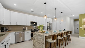 Una cocina moderna con armarios blancos, electrodomésticos de acero inoxidable, una isla de granito y taburetes de bar.