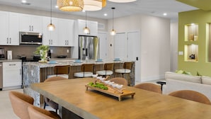 Una cocina moderna con gabinetes blancos, electrodomésticos de acero inoxidable y una mesa de comedor de madera con sillas.