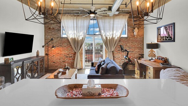 A modern living room with a large TV, a wooden desk, a sofa, and a ceiling fan. - Skyscape - Lofted Luxury Condo Waco/Baylor/Downtown (Waco)