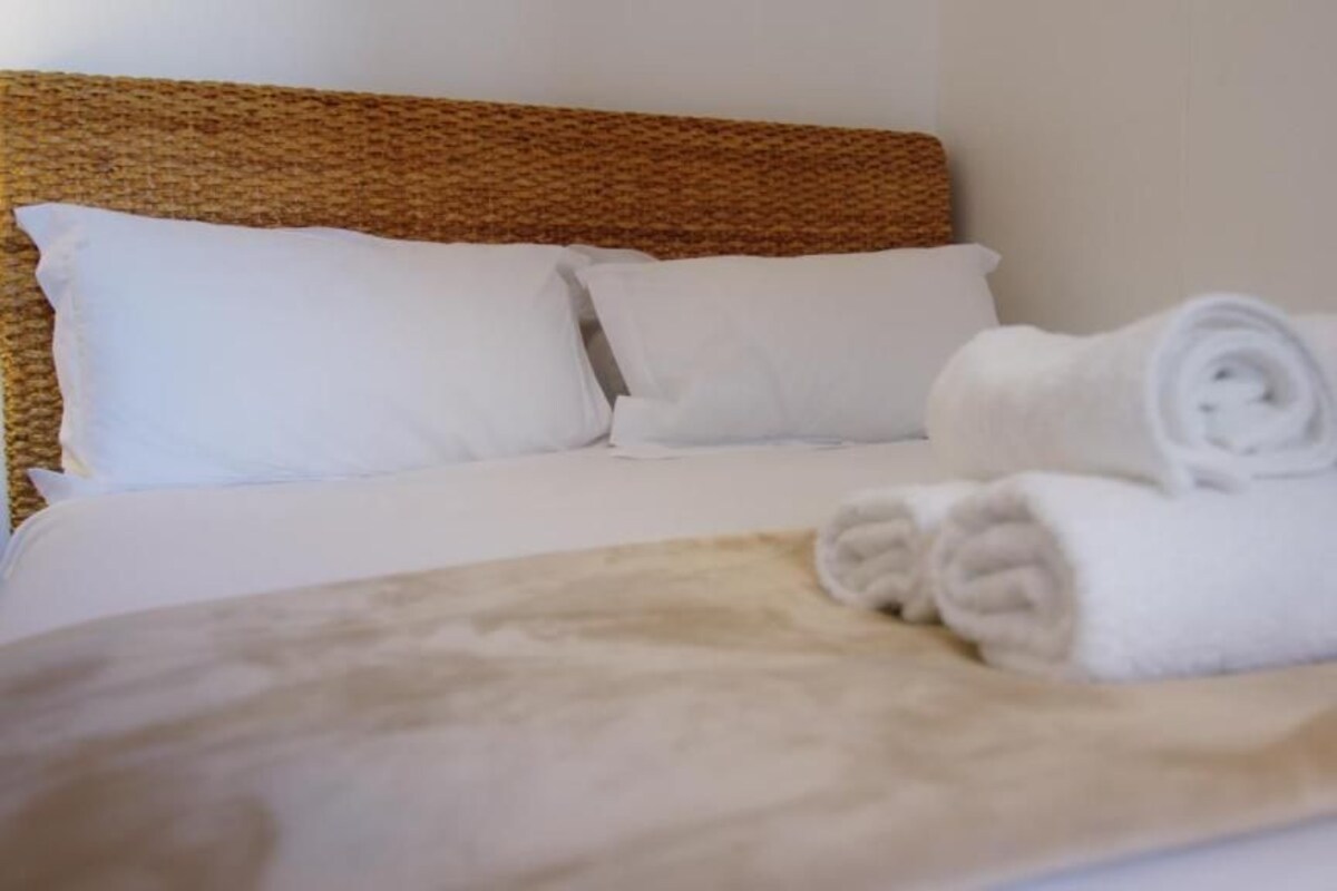 A bed with white linens, a woven headboard, and rolled white towels.