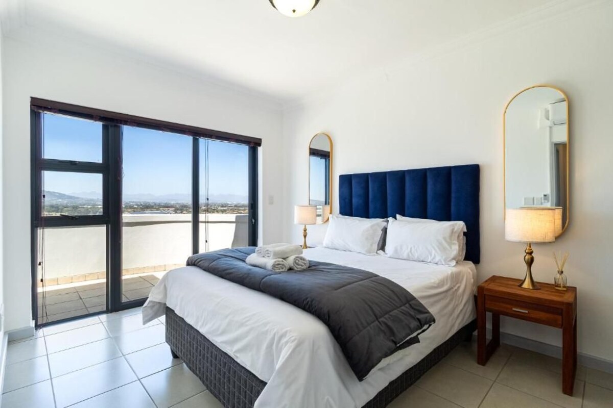 A hotel room with a large bed, two bedside lamps, a mirror, and a view through a sliding door.