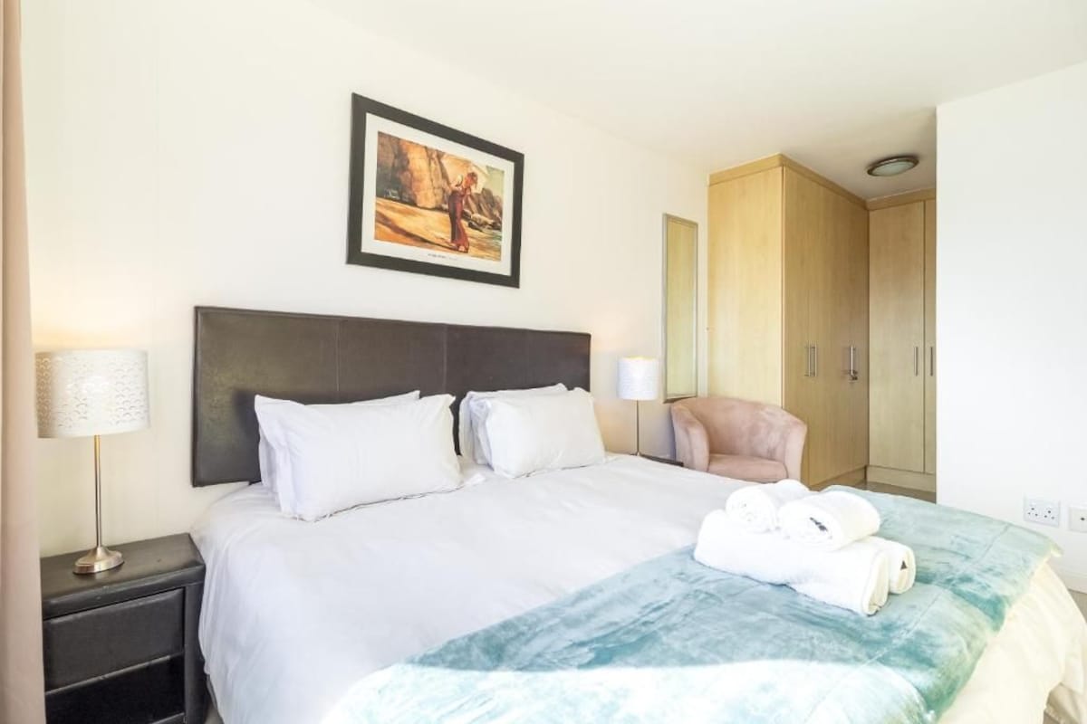 A hotel room with a bed, a chair, a wardrobe, and a painting on the wall.
