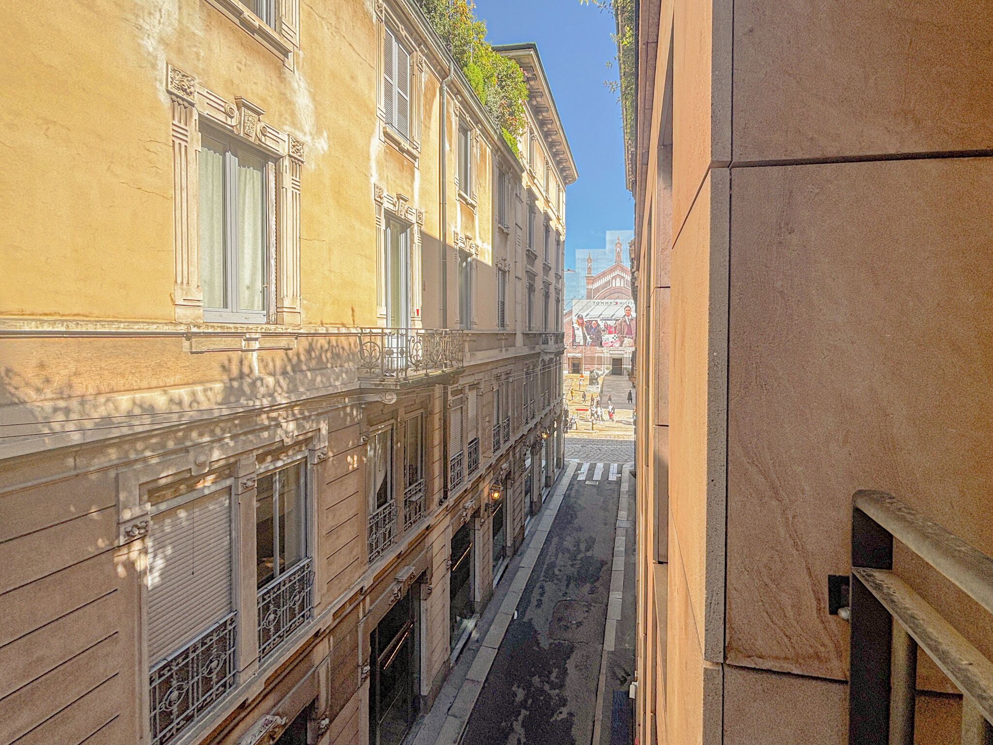 A narrow street with buildings on either side, featuring balconies and windows.